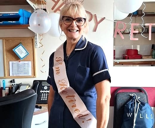 A nurse in uniform wearing a Happy Retirement sash.